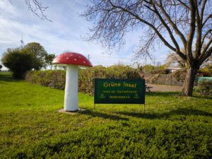 Eingangsbereich des Vereins Gartenfreunde Heddesheim e.V. mit Vereins­schild und großer Fliegenpilzskulptur als markantem Blickfang.